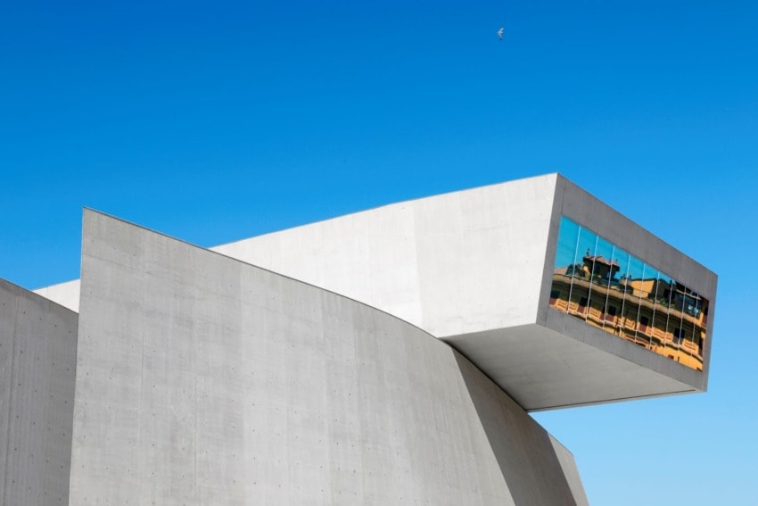 Modern architectural building with angular design, large reflective windows, and a clear blue sky in the background.
