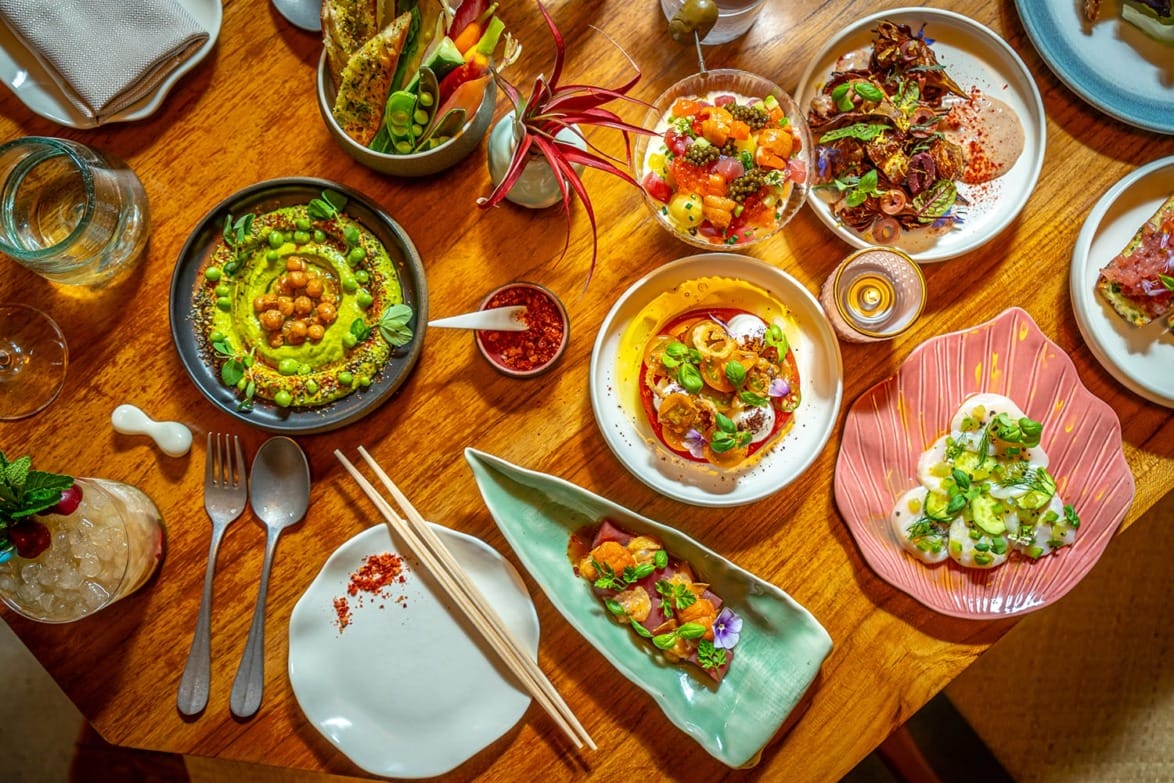 A variety of vibrant, colorful dishes artfully arranged on a wooden table with utensils and decorations.