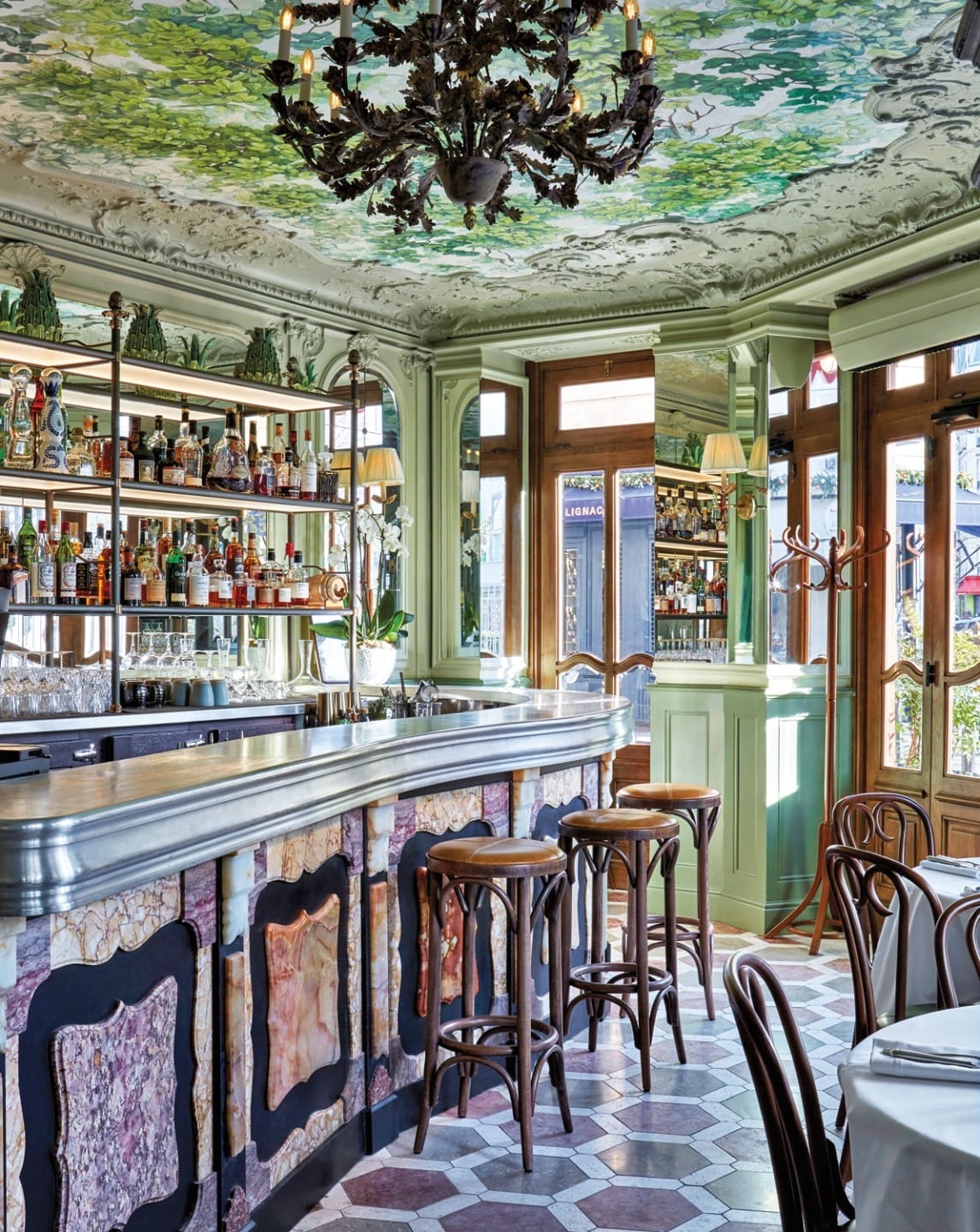 Elegant restaurant interior with a decorative bar, high stools, and a colorful ceiling mural featuring greenery and flowers.