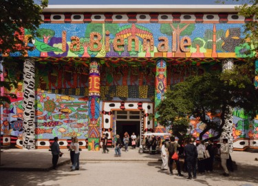 Colorful, vibrant building exterior with decorative patterns and people walking in front on a sunny day.