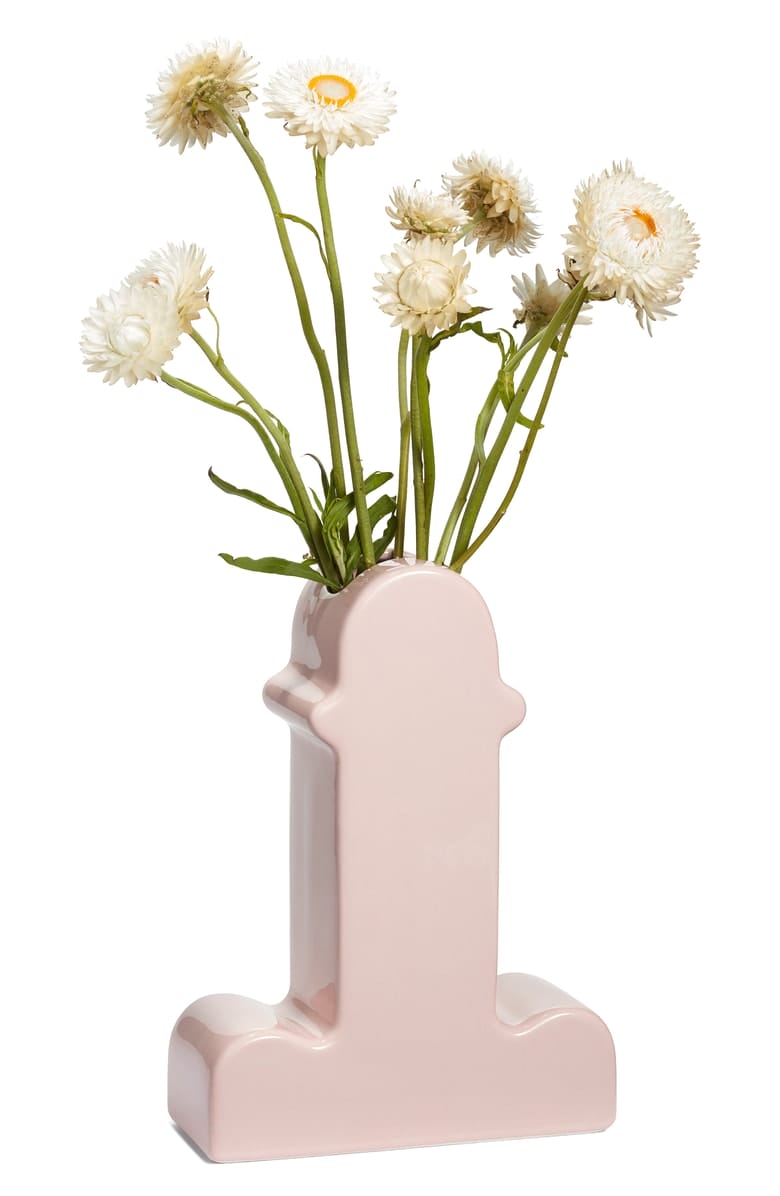 Pink vase shaped like the letter "I" holding white flowers with green stems against a white background.