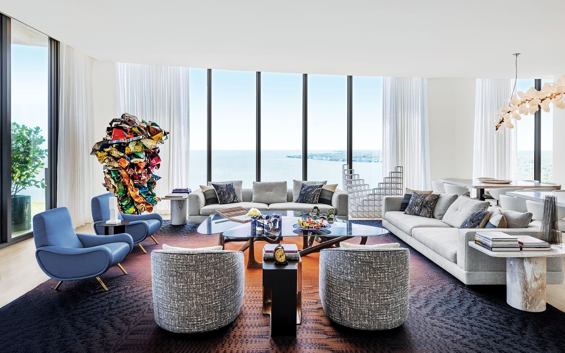 Modern living room with large windows, contemporary furniture, abstract artwork, and ocean view.