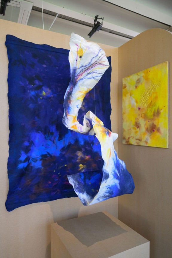 Abstract art installation with vibrant blue fabric and intricate patterns next to a colorful yellow and orange canvas.