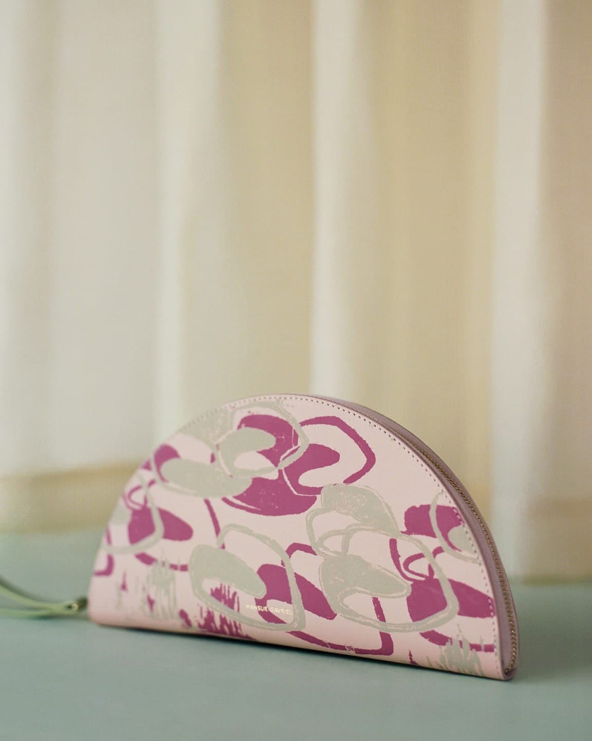 Pink and white half-circle clutch with abstract floral design on a soft, pastel background.