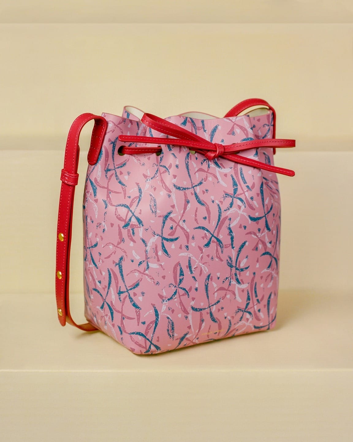Pink and red patterned handbag with a bow and adjustable strap on a neutral background.