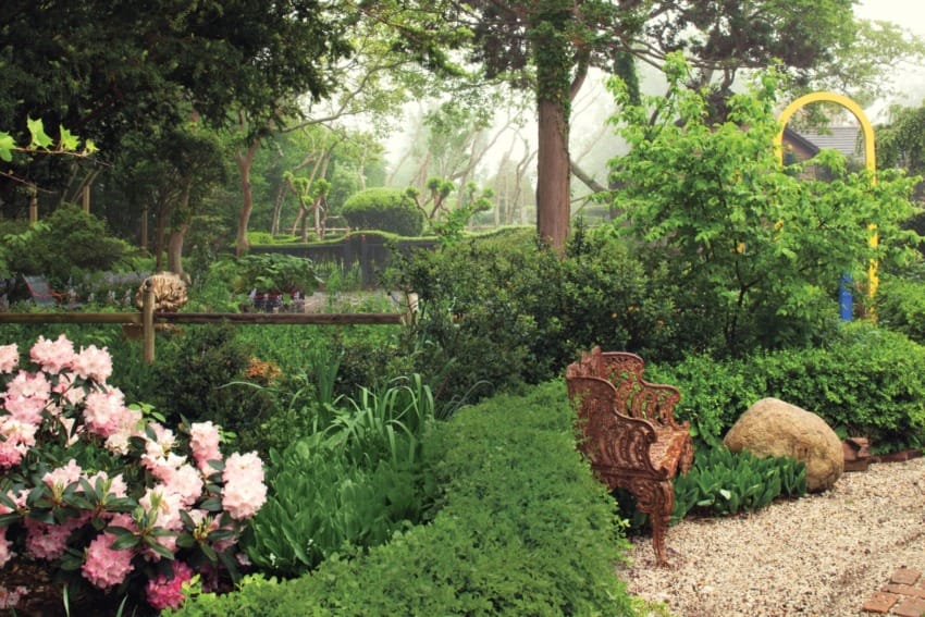 lush green garden with ornate bench surrounded by blooming flowers and trees on a foggy day