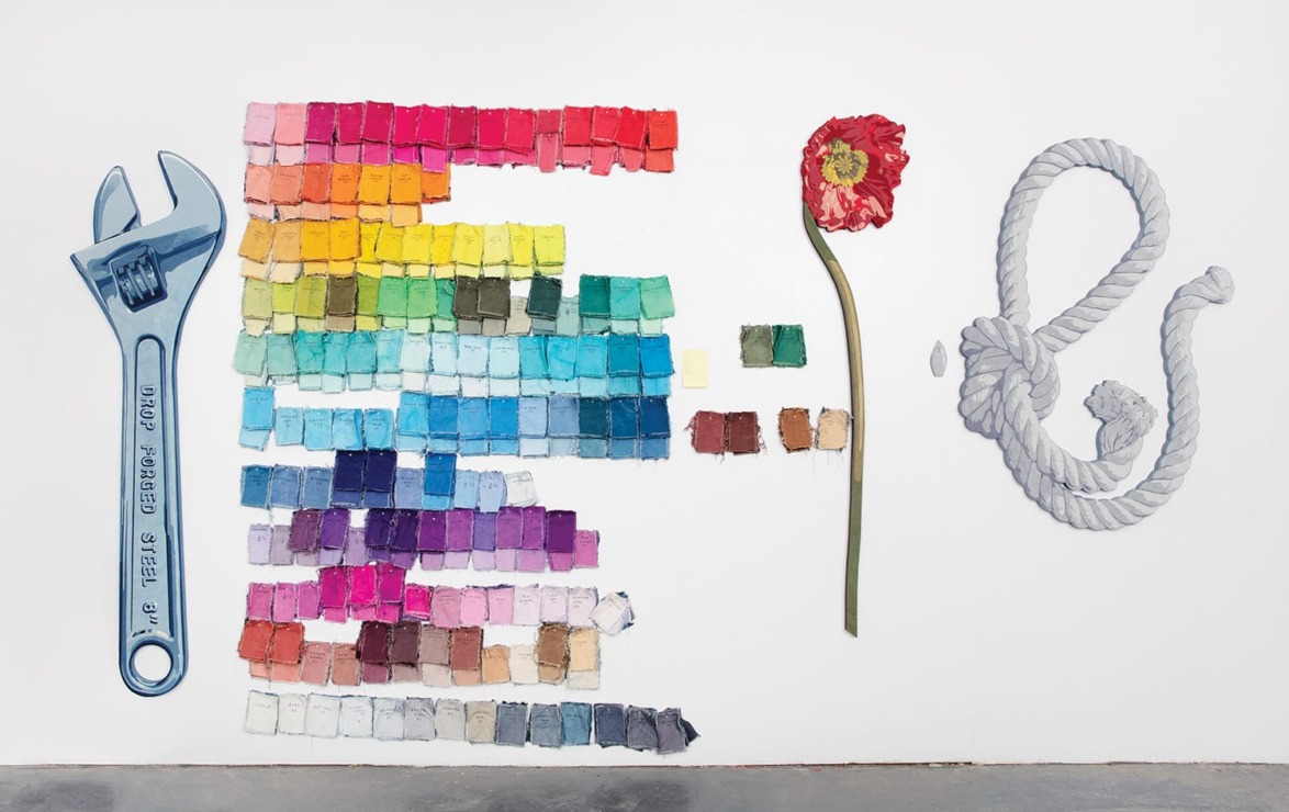 Colorful paint swatches, wrench, red flower, and rope arranged artistically against a plain white wall.