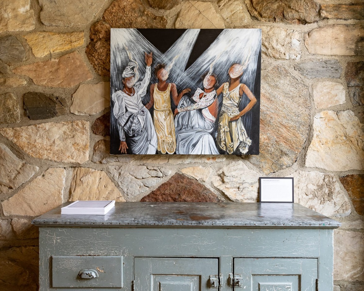 Painting of five abstract figures on a stone wall above a blue wooden cabinet with two stacks of paper.