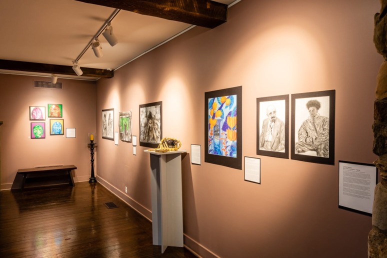 Art gallery interior with various framed artworks on walls, a sculpture on a pedestal, and hardwood floors.