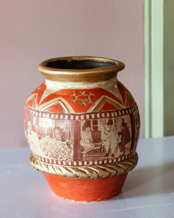 Ancient-style ceramic vase with red geometric patterns and etched human figures on a light background.