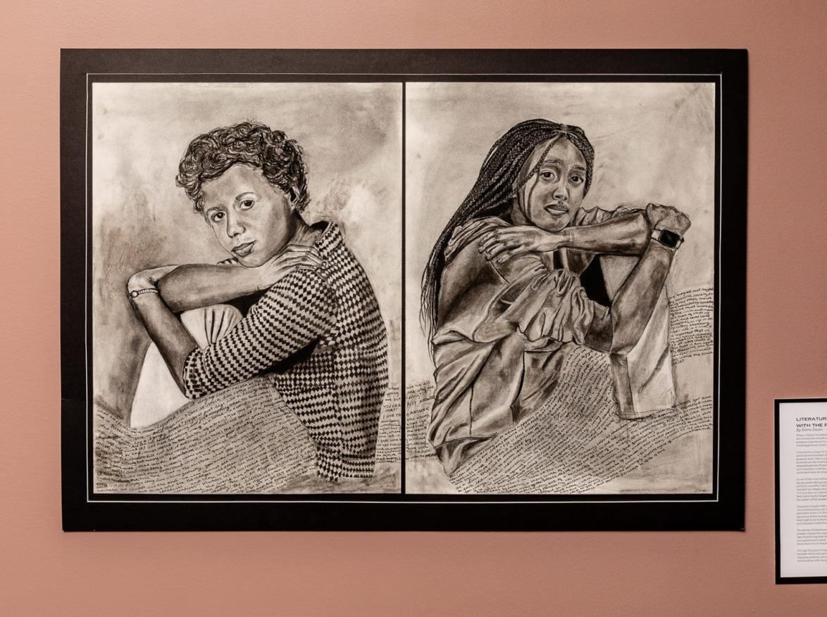 A framed artwork with two people sitting side by side, drawn with detailed pencil shading.