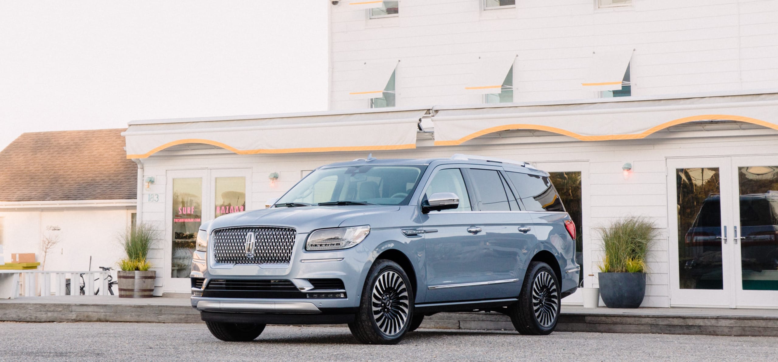 Silver SUV parked in front of a white house with large windows and potted plants.