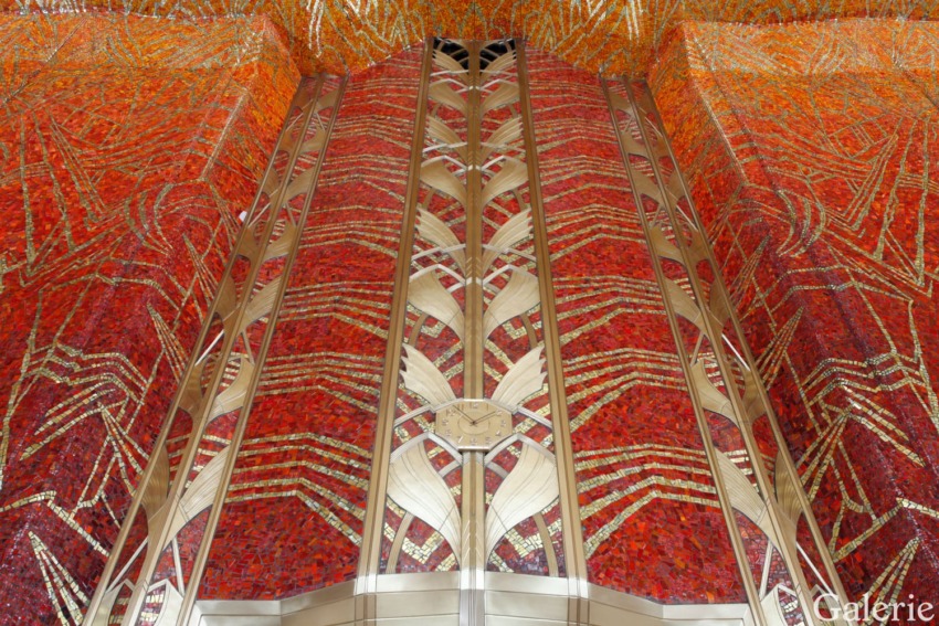 Art Deco mosaic above golden elevator doors in vibrant red, gold, and orange tones at the Chrysler Building, New York.