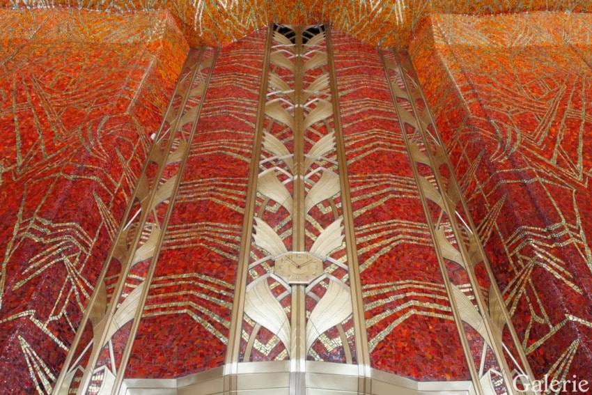 Art Deco mosaic above golden elevator doors in vibrant red, gold, and orange tones at the Chrysler Building, New York.