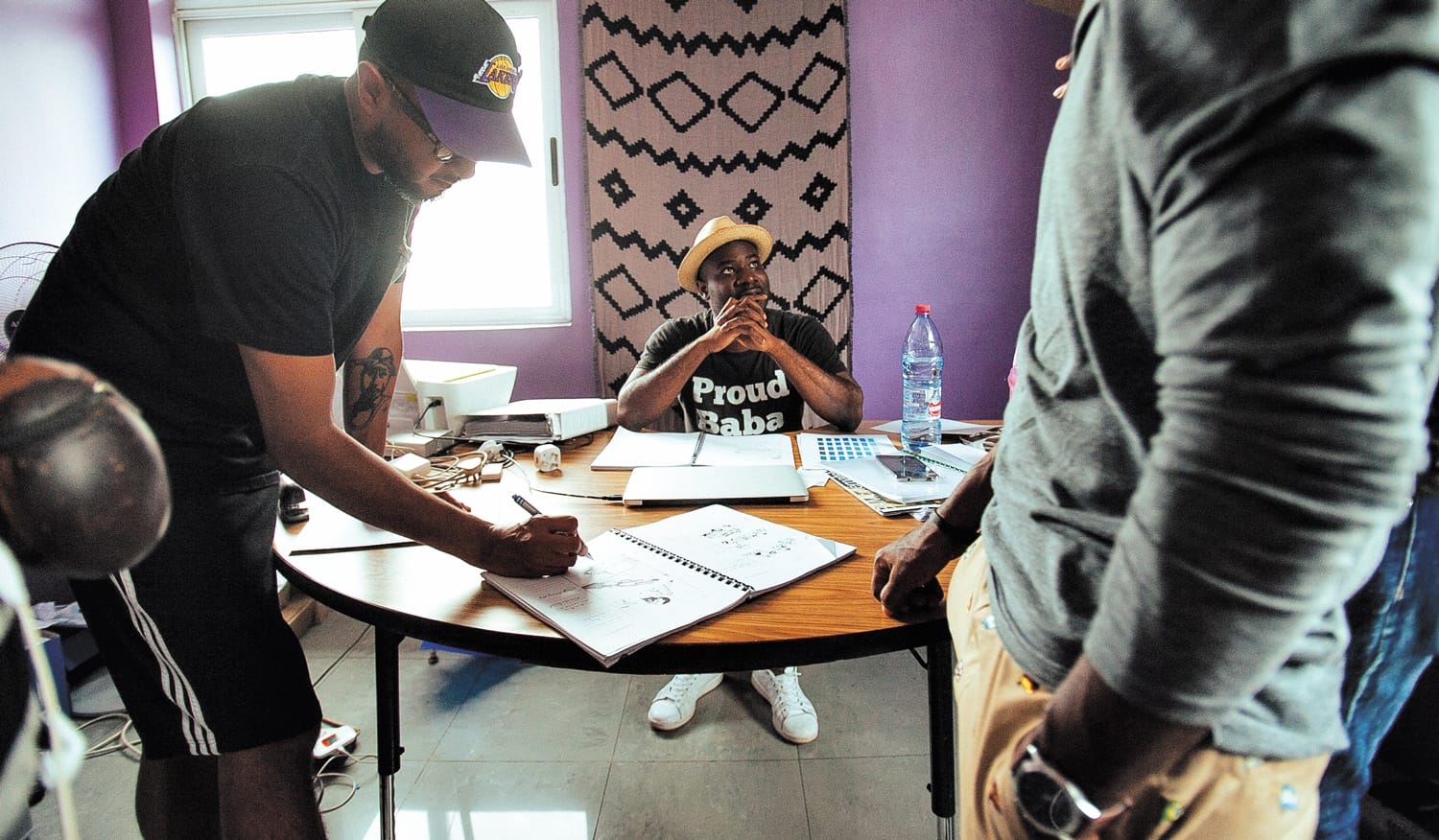 Group of people collaborating at a round table with sketches and notes in a brightly lit room.