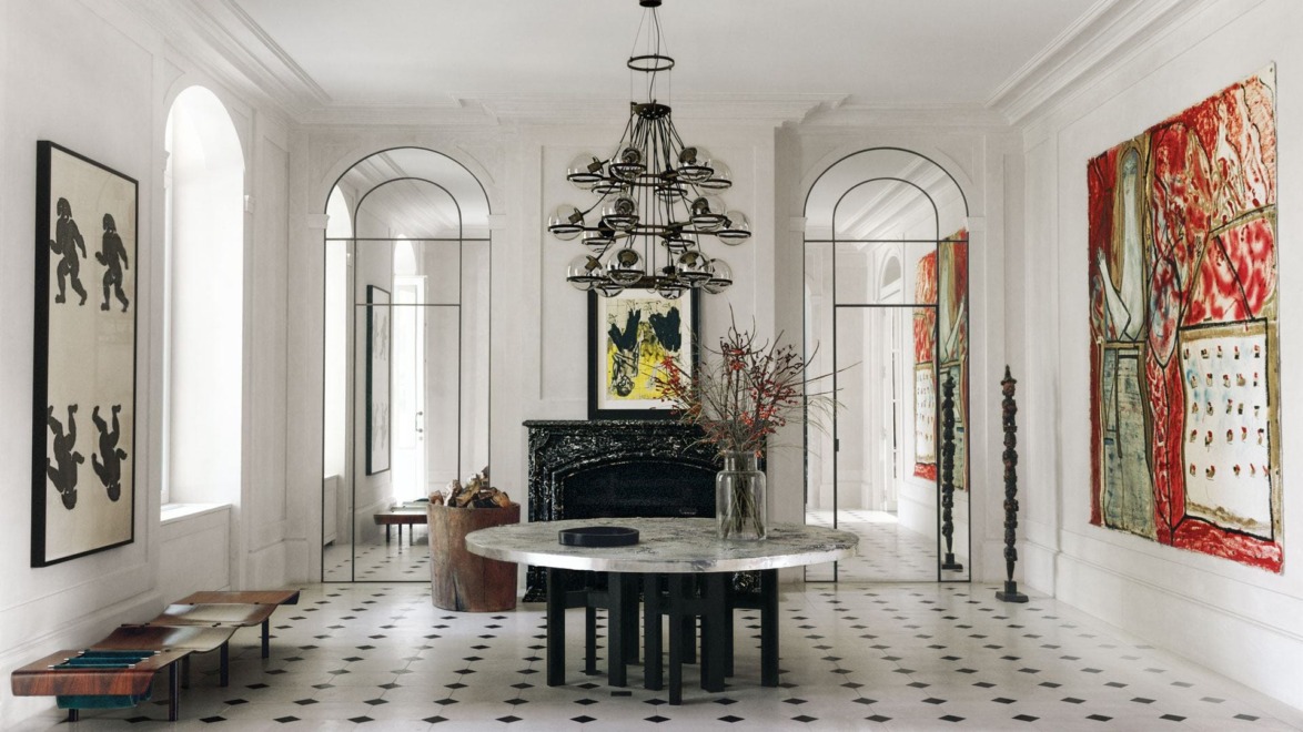Elegant dining room with marble table, modern chandelier, abstract art, black fireplace, and large windows.