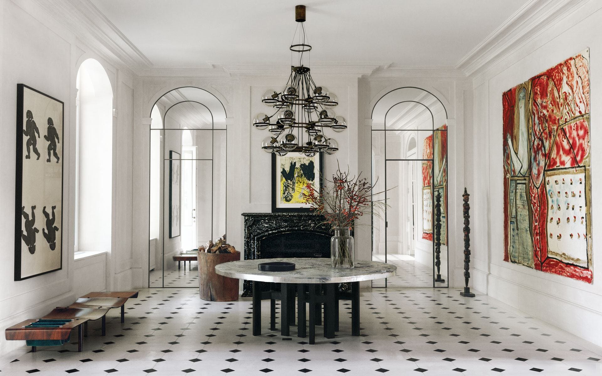 Elegant dining room with marble table, modern chandelier, abstract art, black fireplace, and large windows.