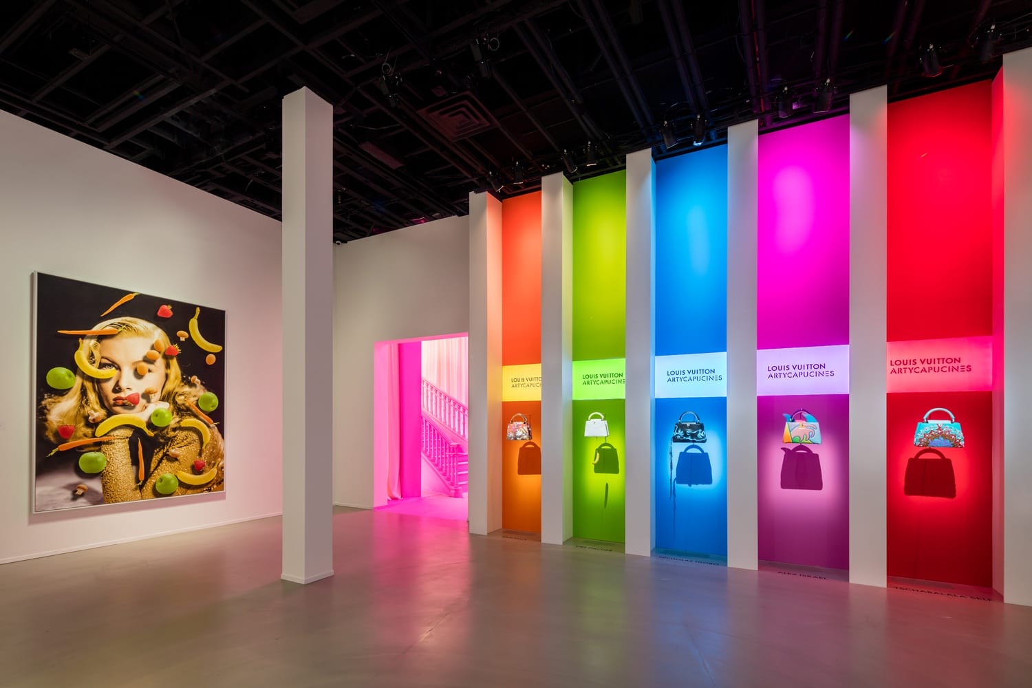 Colorful display of Louis Vuitton bags on vibrant vertical panels in a modern art exhibit setting.