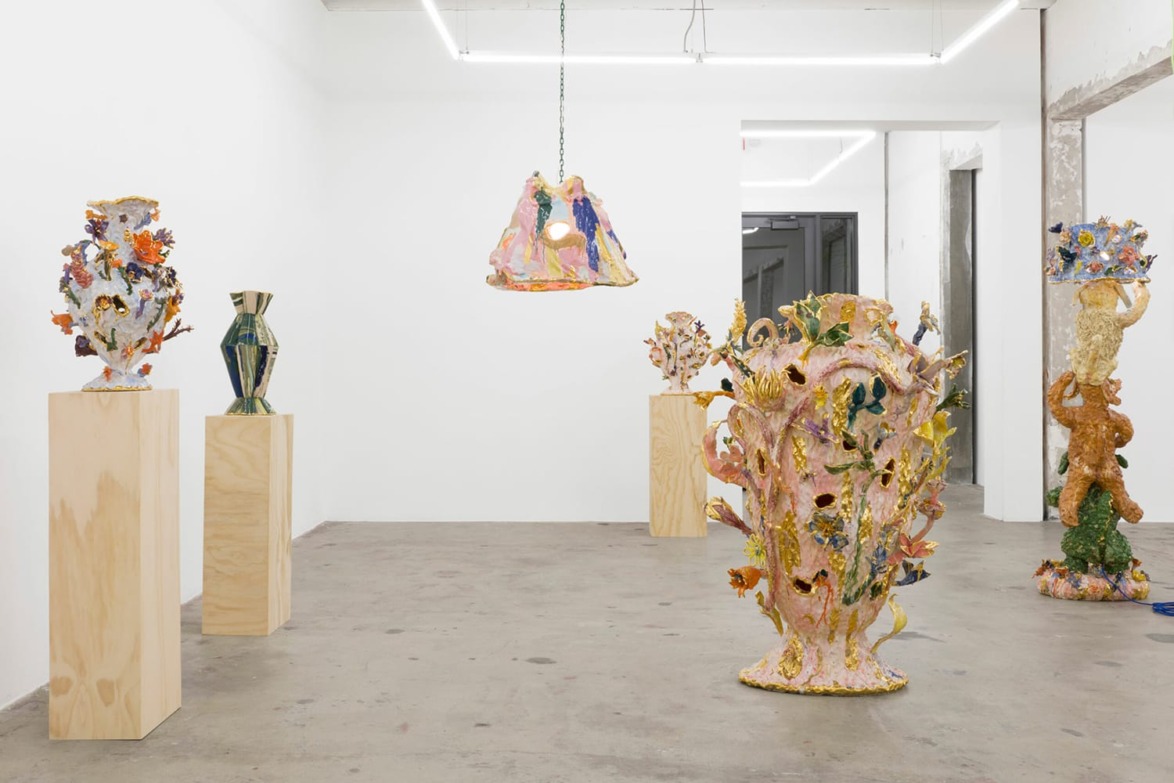 Art gallery displaying colorful ceramic sculptures on wooden pedestals in a minimalist room with concrete floor.