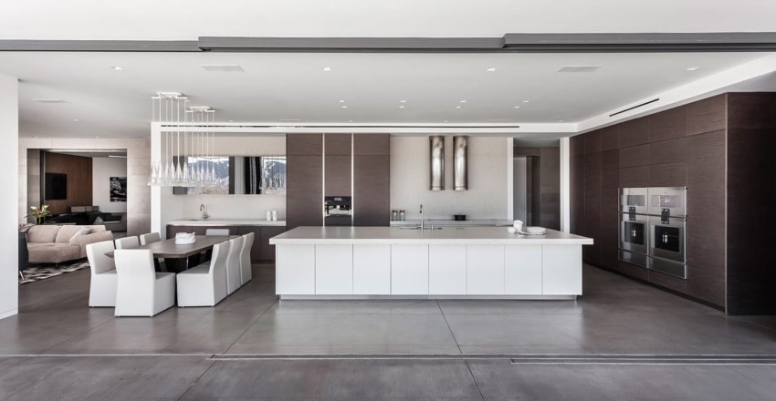 Modern kitchen with large island, white and brown cabinetry, sleek lighting, and integrated appliances.