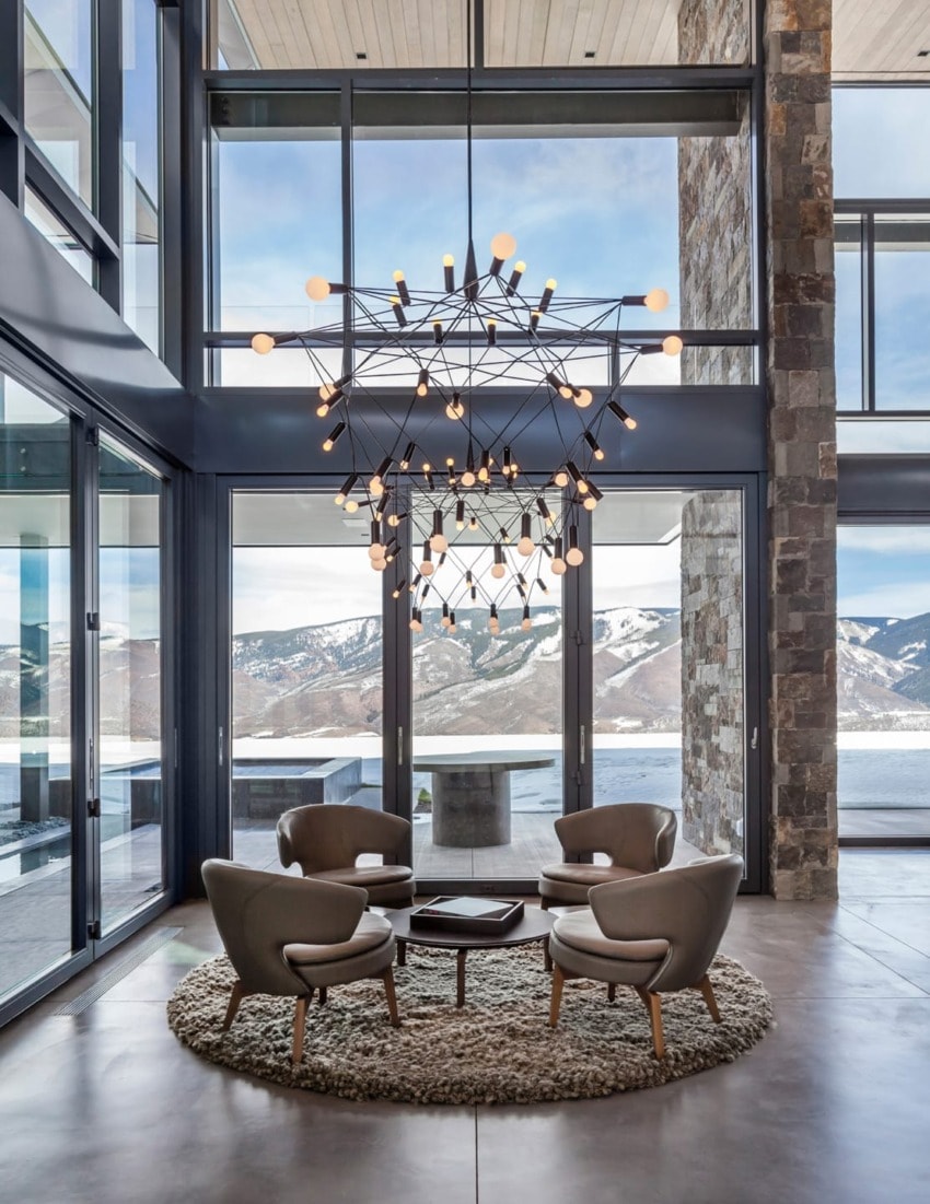 Modern interior with four chairs around a table, chandelier above, large windows showcasing a snowy mountain landscape.