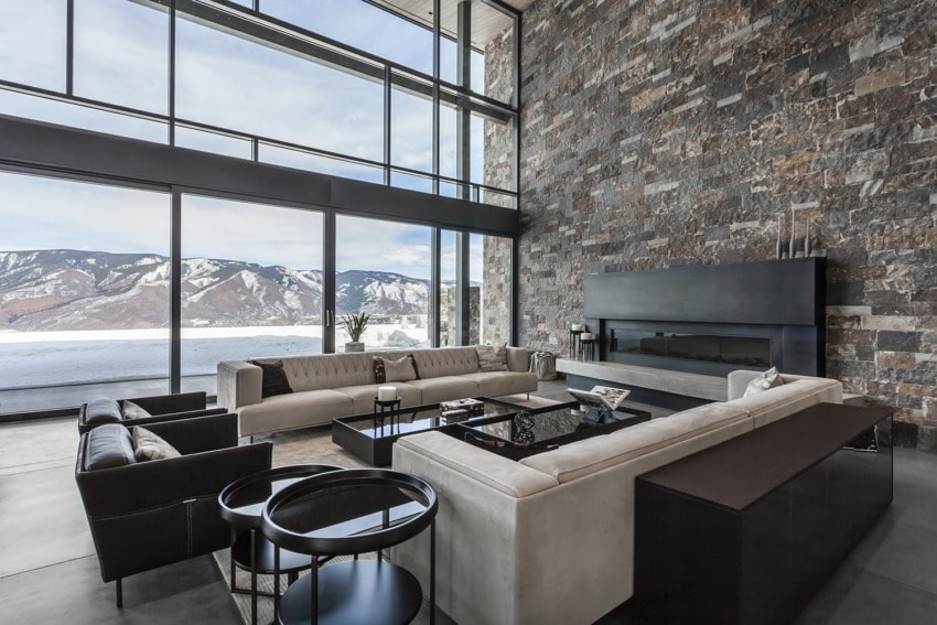 Modern living room with large windows, mountain view, stone wall, and sleek furniture.
