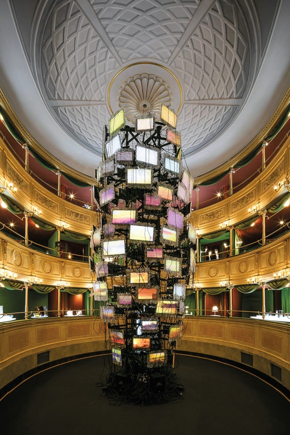 Tall sculpture of stacked screens with wires in a large, ornate, circular room with a domed ceiling and gold accents.