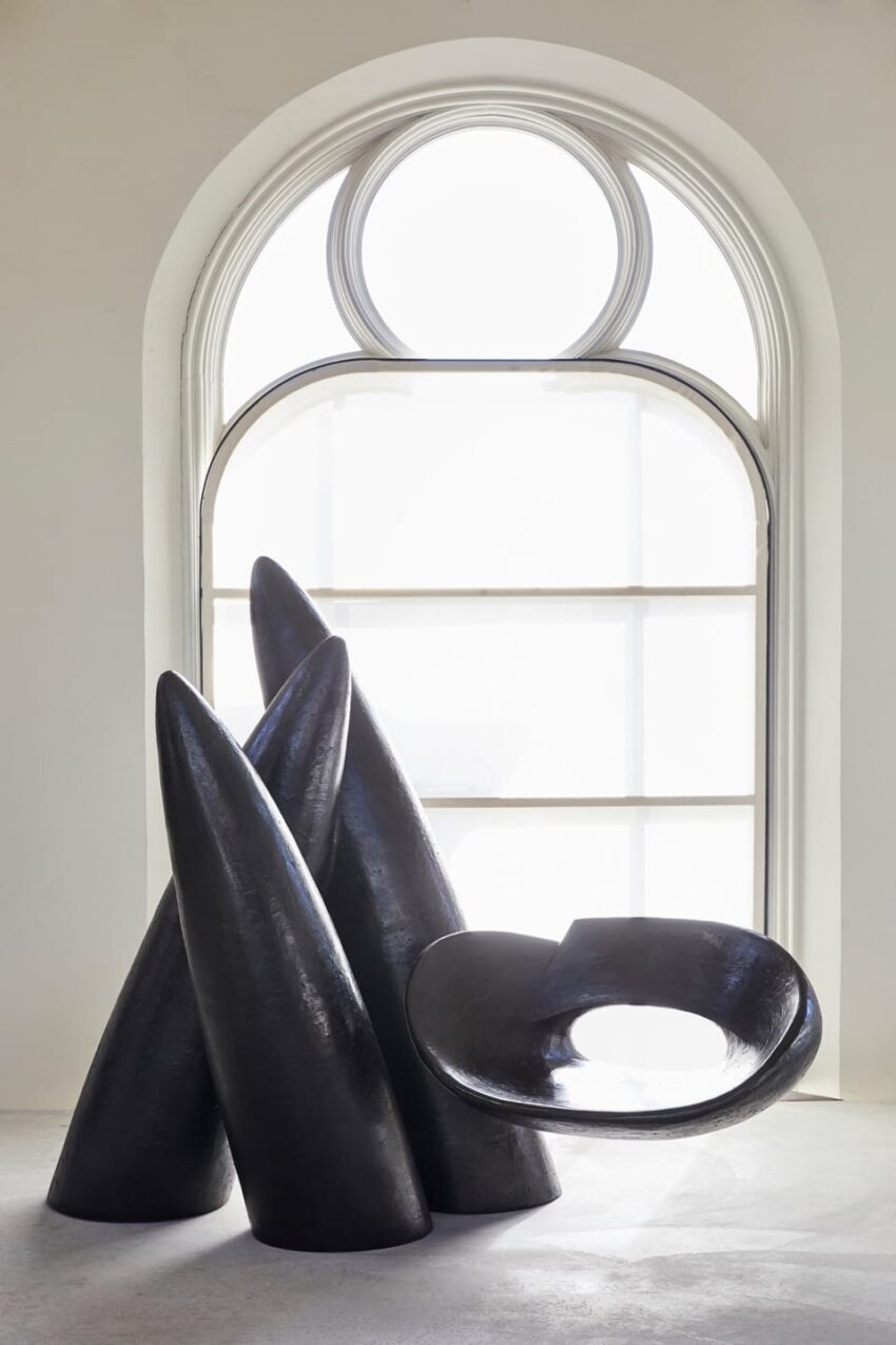 Abstract black sculptures in front of a large arched window with a soft light filling the room.