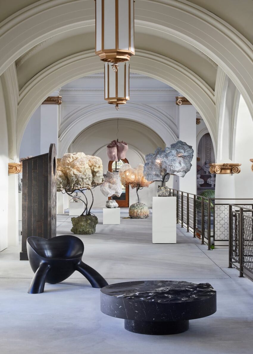 Contemporary art exhibition in a grand arched gallery with sculptures and modern furniture.