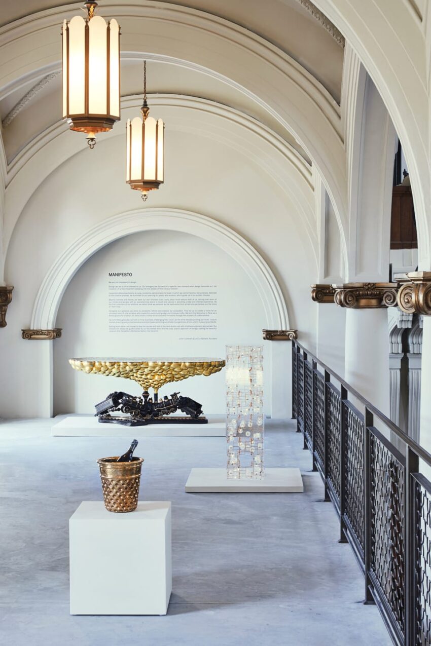 Museum exhibition with sculptures on display under ornate arches and hanging chandeliers.