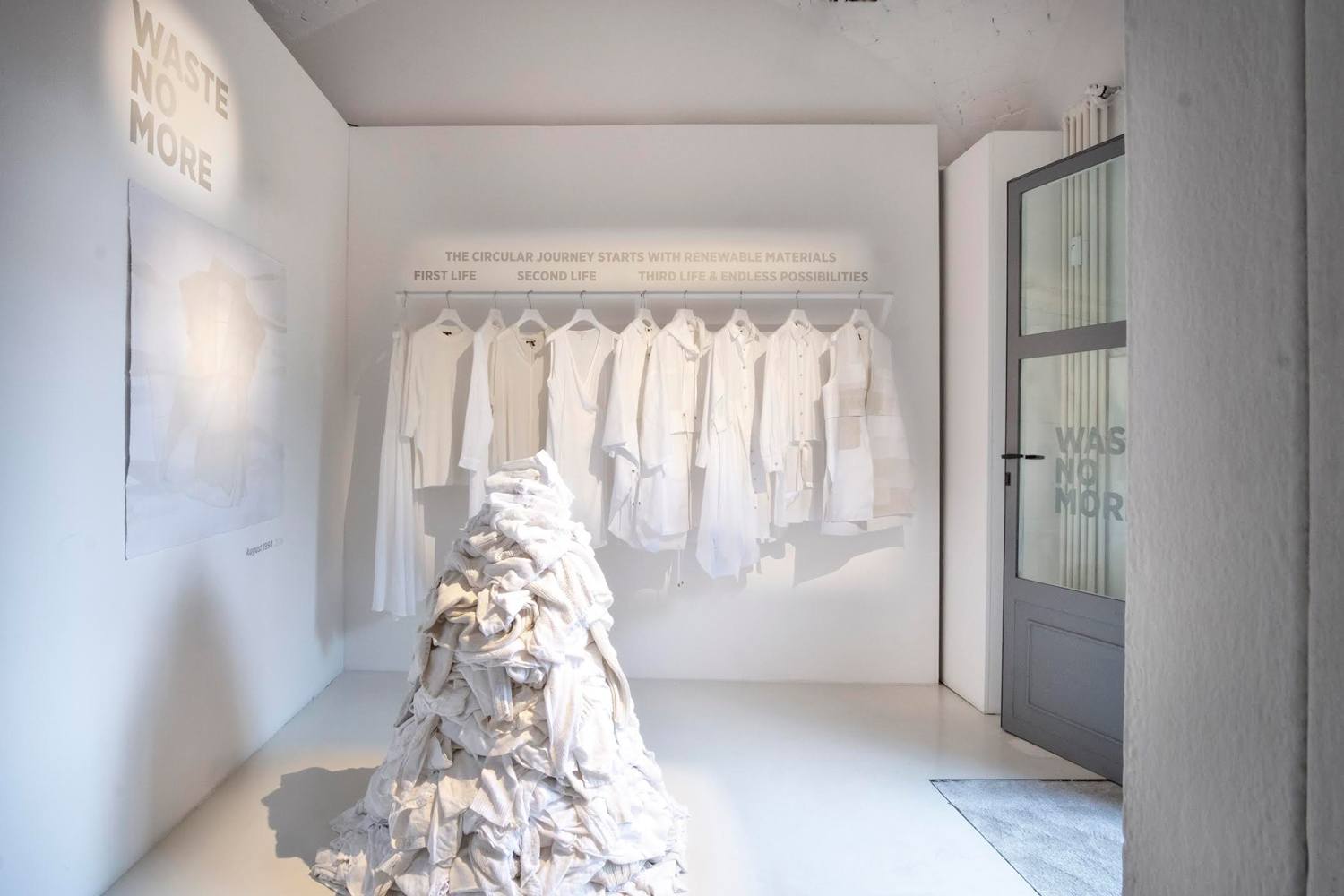 Exhibit of white clothes hanging and text about circular fashion journey with renewable materials on the wall.