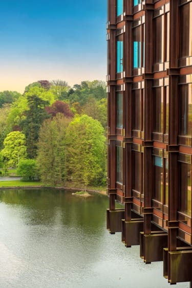 Modern building overlooking a serene lake and lush green trees under a clear blue sky.