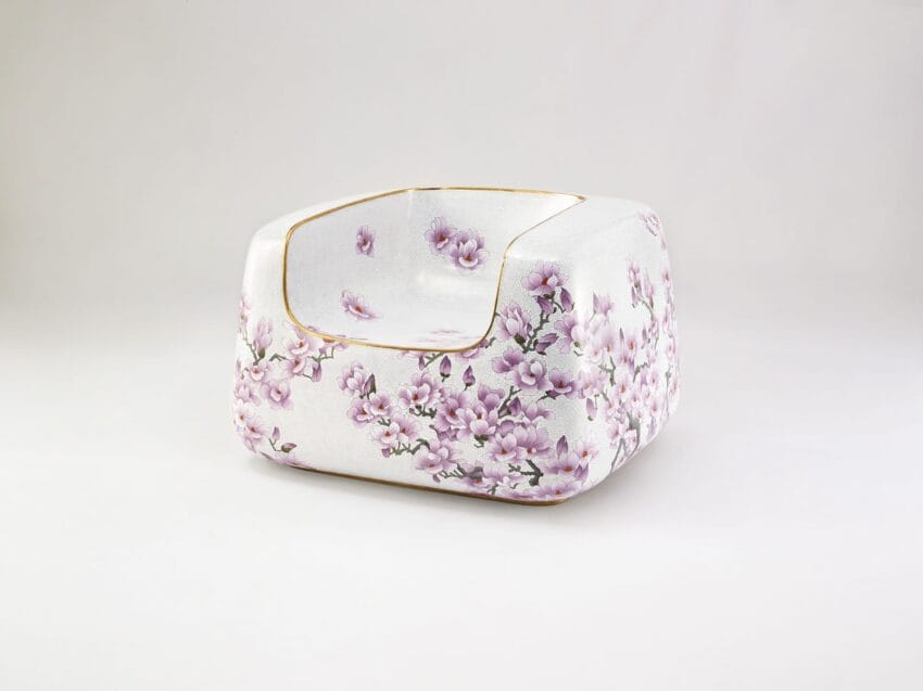 White porcelain chair with delicate pink floral pattern and gold accents against a plain background.