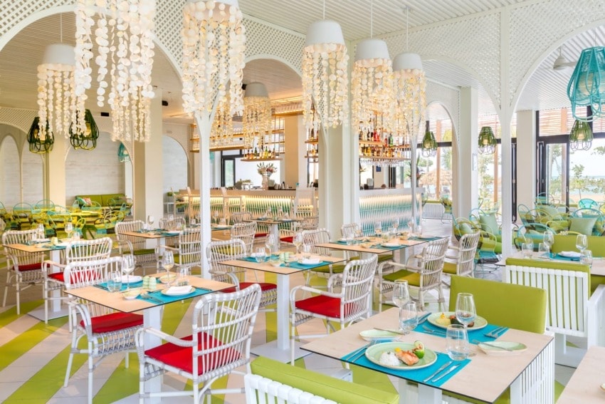 Colorful beachside restaurant interior with white chairs, vibrant decorations, and set tables, creating a vibrant dining atmosphere.