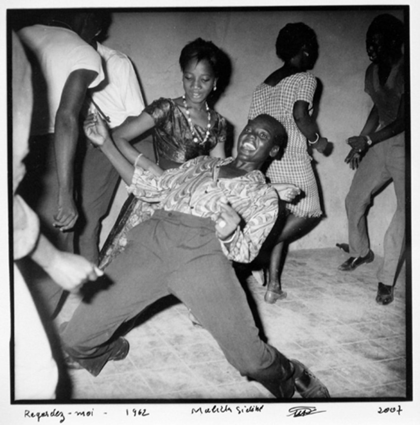 People dancing energetically at a lively party, with one man leaning back joyfully on the dance floor.