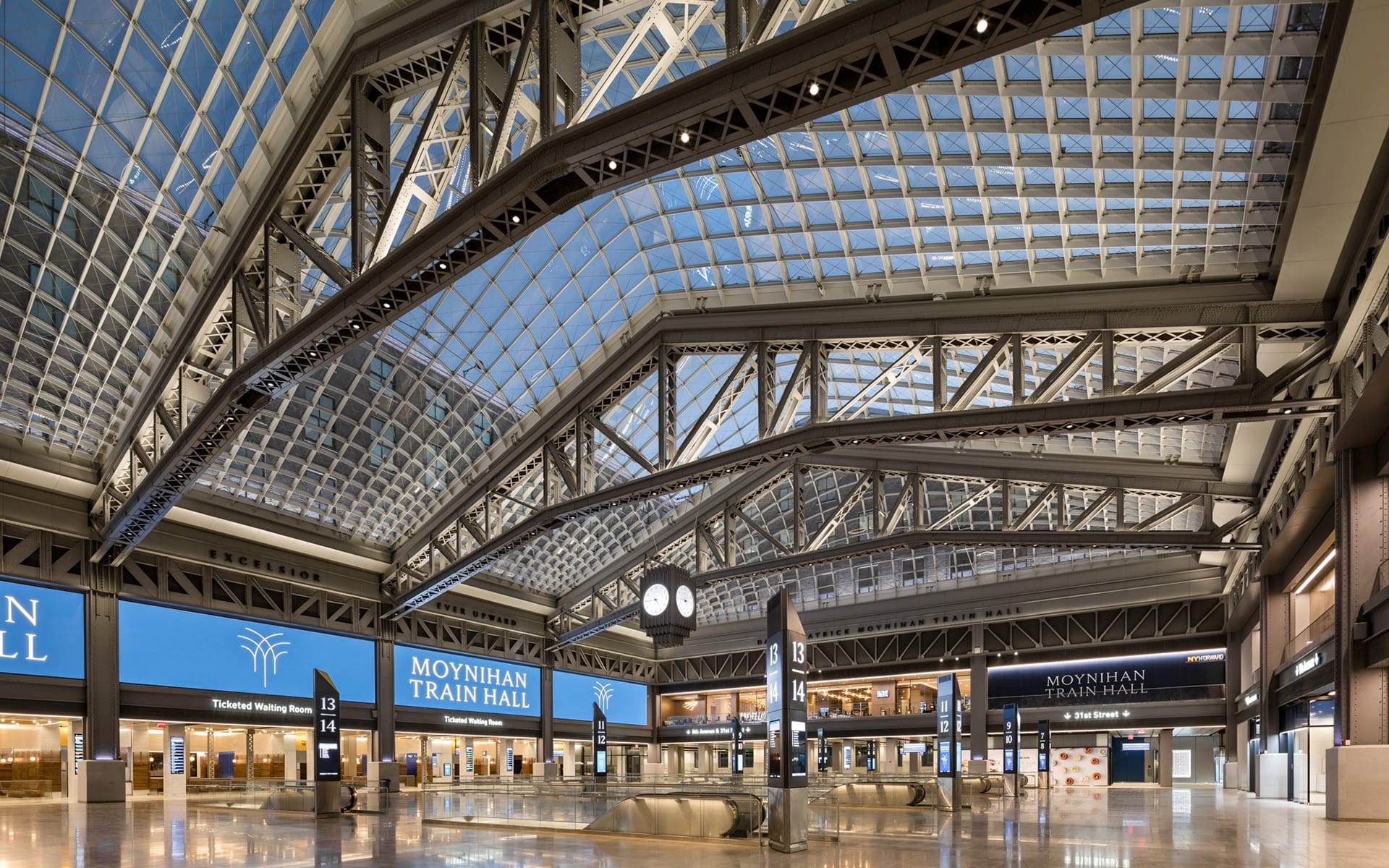 Interior view of Moynihan Train Hall featuring a spacious glass ceiling, information displays, and an iconic clock.