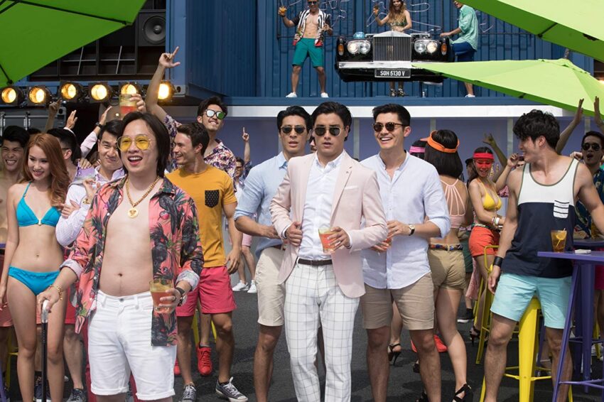 A group of people enjoying a lively outdoor party, with men in suits and casual attire, and women in swimwear.