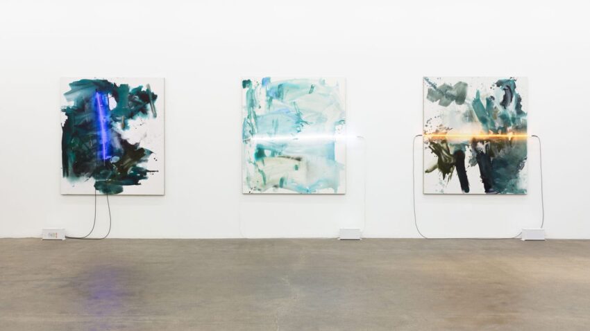 Abstract paintings with vibrant colors and neon light accents displayed on a gallery wall.