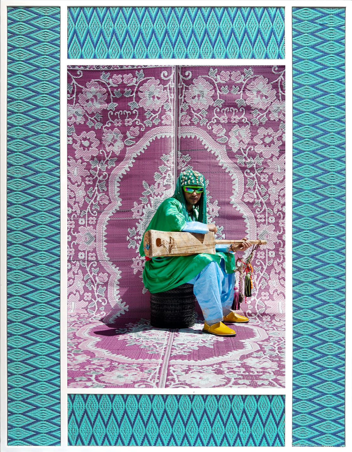 Person in green attire playing a string instrument, sitting in front of a patterned pink and purple backdrop.
