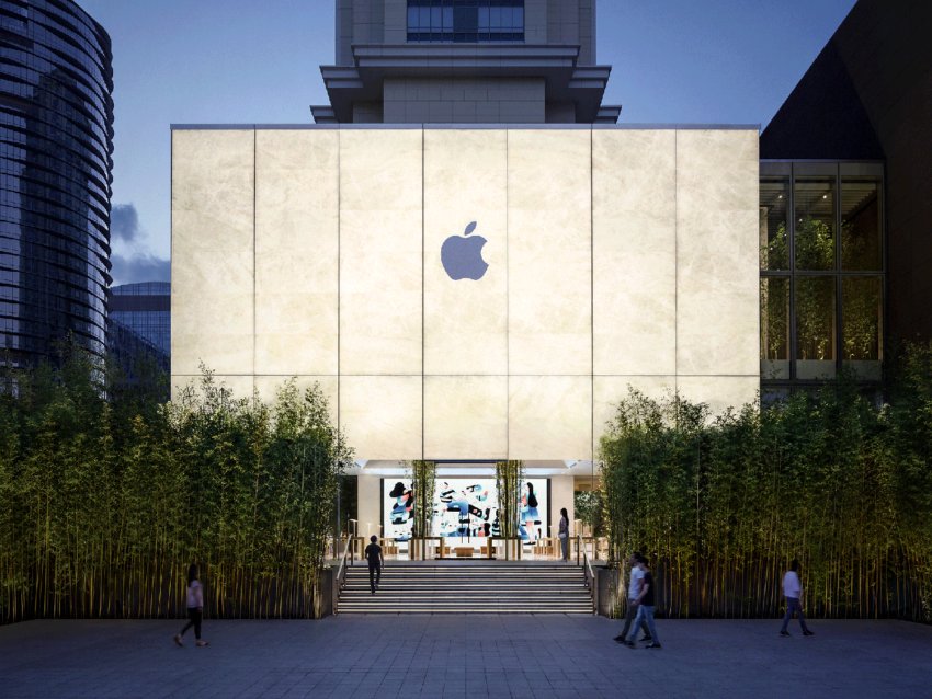 Exterior of a modern flagship store with an illuminated facade, large glass entrance, and surrounding bamboo plants at dusk.