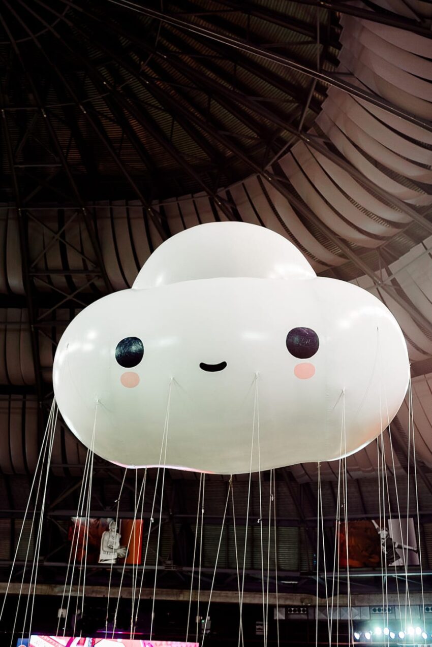 Cute cloud-shaped balloon with a smiling face floating inside a large indoor venue.