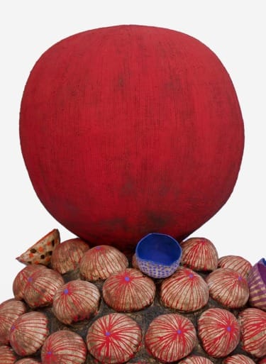 Contemporary sculpture with a large red sphere atop textured circular forms, adorned with small colorful patterns.