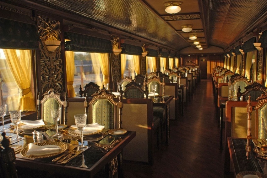 Luxurious vintage train dining car with ornate decor, elegant table settings, golden curtains, and warm lighting.