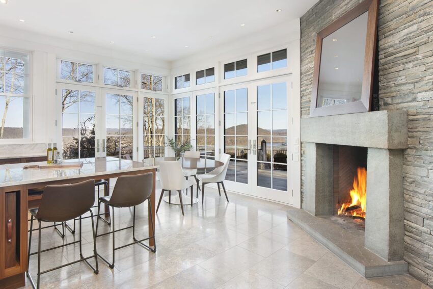 Contemporary dining area with fireplace, large windows, high chairs, and marble flooring offering a scenic view.