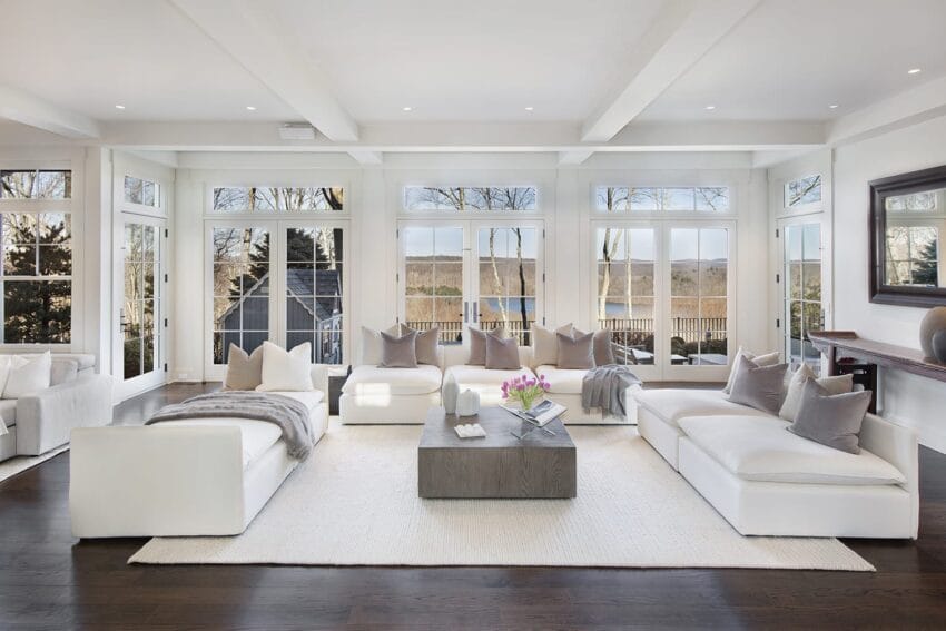 Modern living room with large windows, white sofas, dark wood floor, and a coffee table, overlooking a scenic outdoor view.