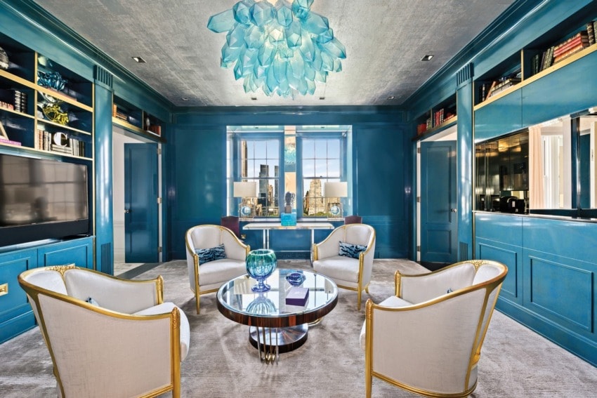 Luxurious blue-themed room with elegant chairs, round glass table, and decorative chandelier.