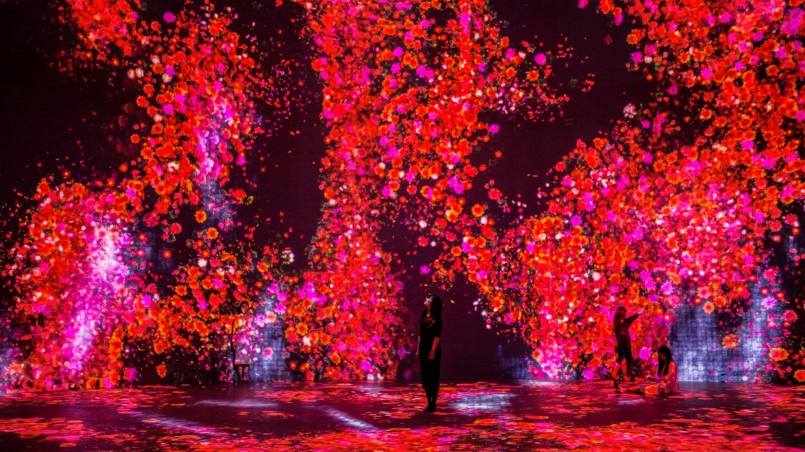 Vibrant digital art installation with cascading red and pink floral patterns surrounding silhouettes of people in an immersive experience.