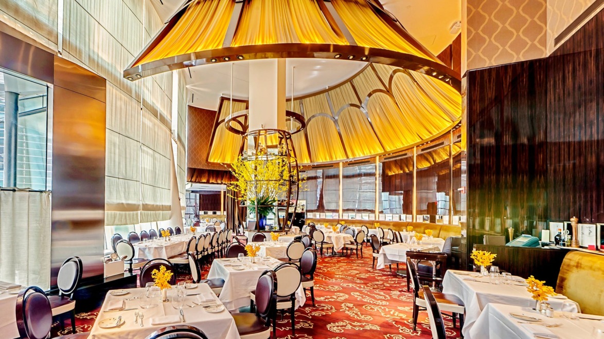 Elegant restaurant interior with luxurious decor, round tables set with white tablecloths, and a large circular chandelier.