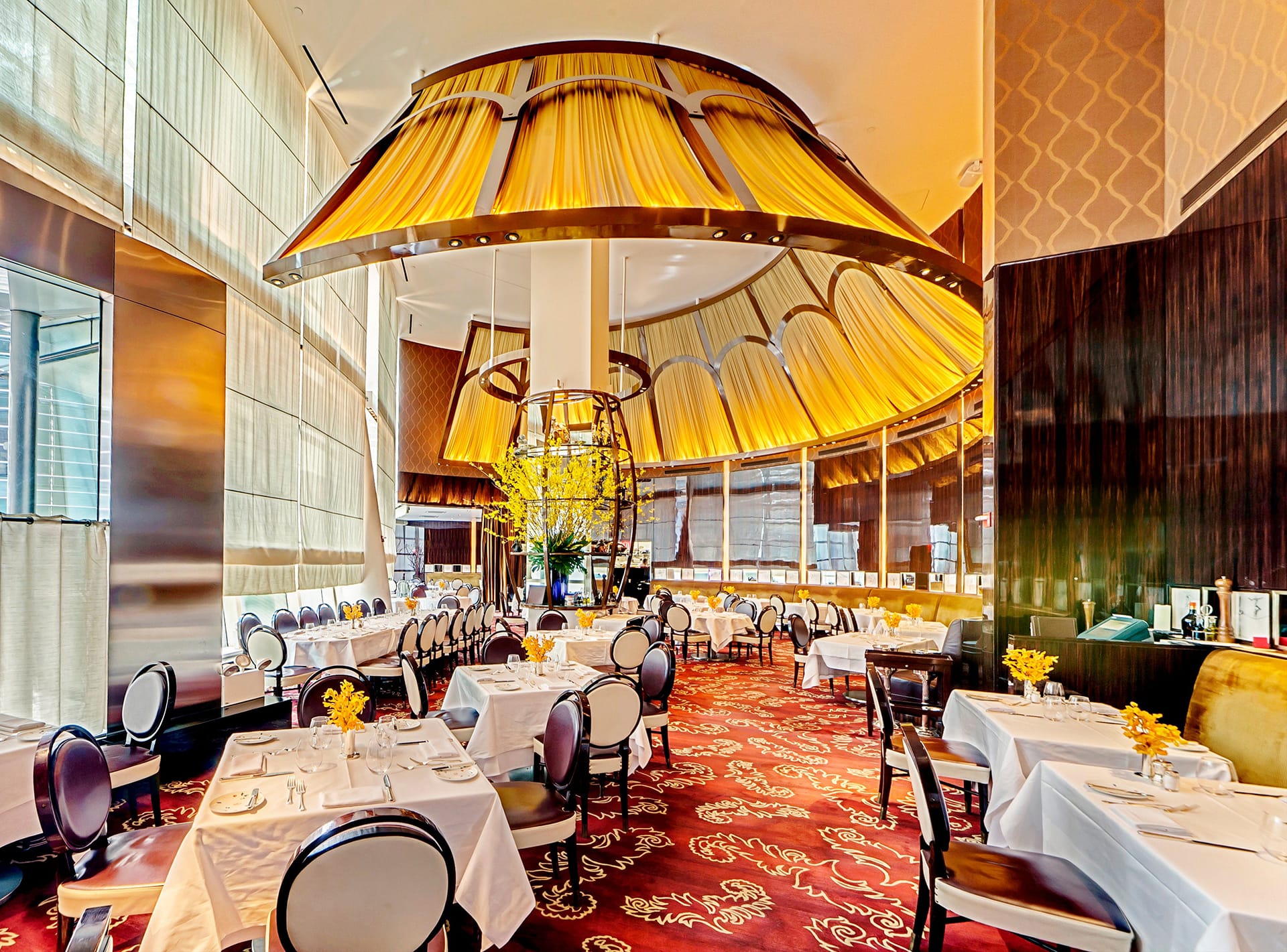 Elegant restaurant interior with luxurious decor, round tables set with white tablecloths, and a large circular chandelier.