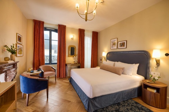 Hotel room with a large bed, elegant decor, a seating area, and a window with red curtains and vintage-style lighting.